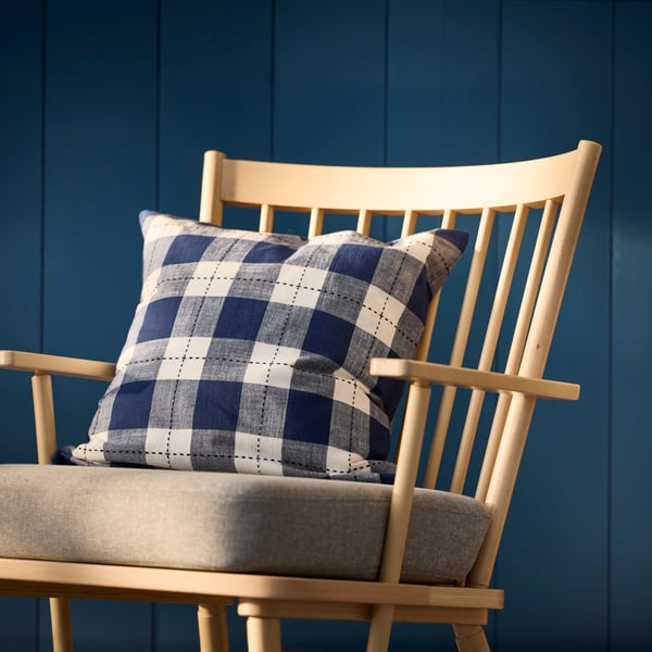 A beige PERSBOL armchair with a dark blue SVAMPFLY cushion cover, set against a dark blue wooden wall.