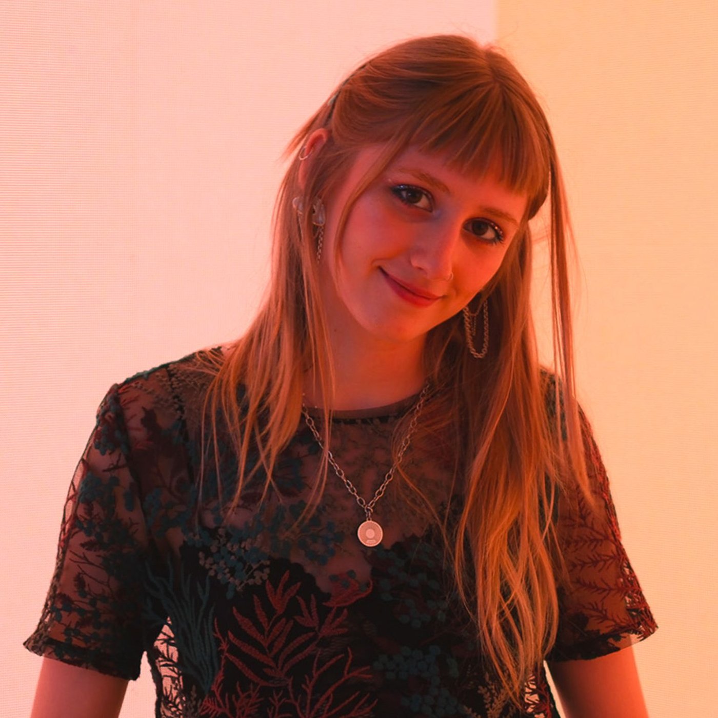 Während der Mailänder Designwoche 2024 steht Rea am IKEA Standort auf einer Bühne. Sie trägt ein schwarzes T-Shirt und eine Halskette. Im Hintergrund ist eine digitale Anzeige in sanftem Rot zu sehen.