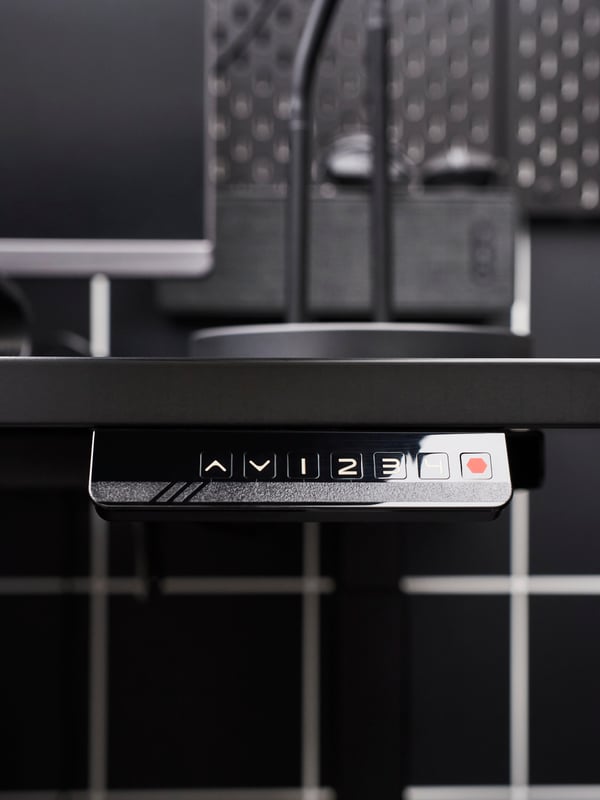 The front and controller of an UPPSPEL gaming desk against a black and white grid.