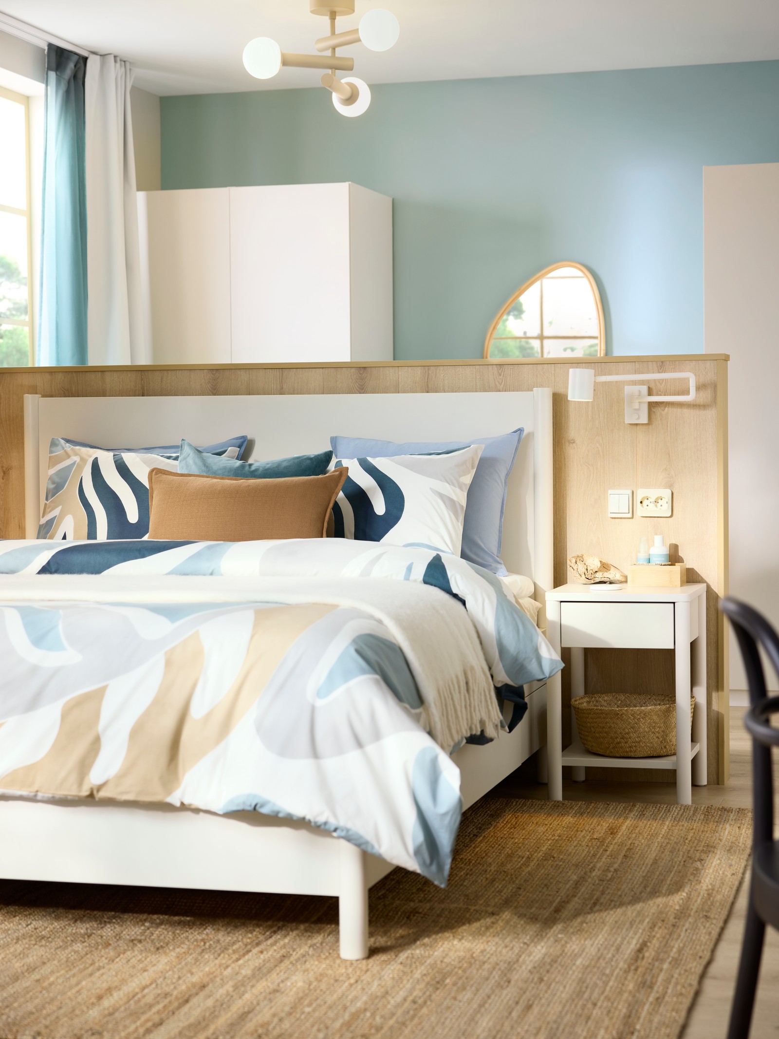 A beachy-feeling hotel room has an off-white TONSTAD bed frame with storage and a headboard against a low wooden accent wall.