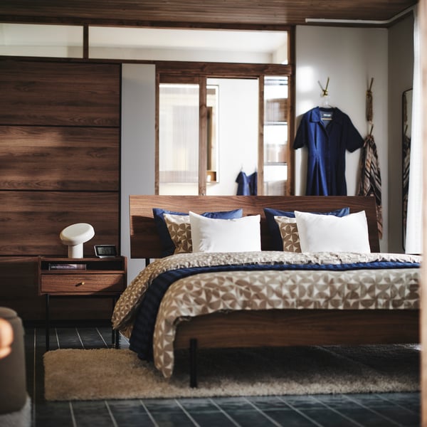 The RÅDMANSÖ series in a bedroom with an overall warm brown colour, blue and beige. Focus on bed, bedside table.