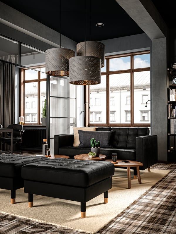 A sitting area by the window with a black leather sofa, three large hanging lamps and wooden coffee tables.