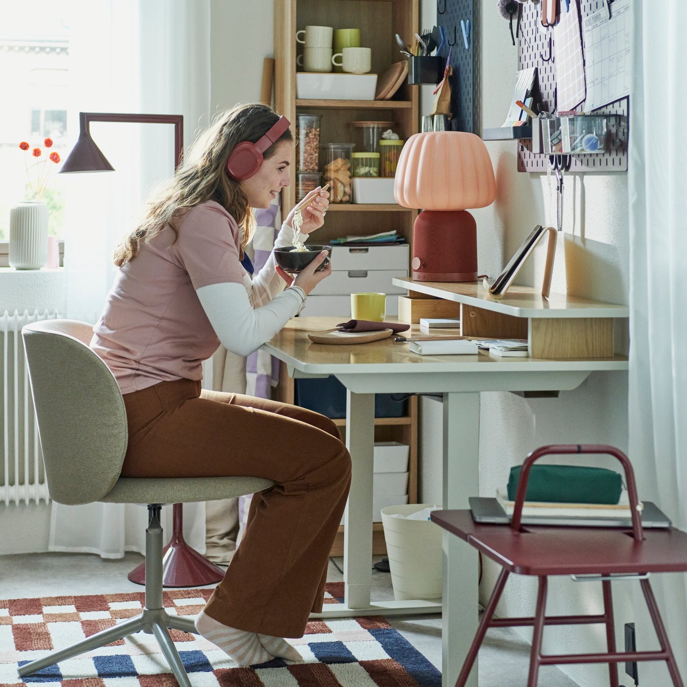 En person sitter vid ett skrivbord med hörlurar och använder mobiltelefon i en färgstark och personlig arbetsmiljö.