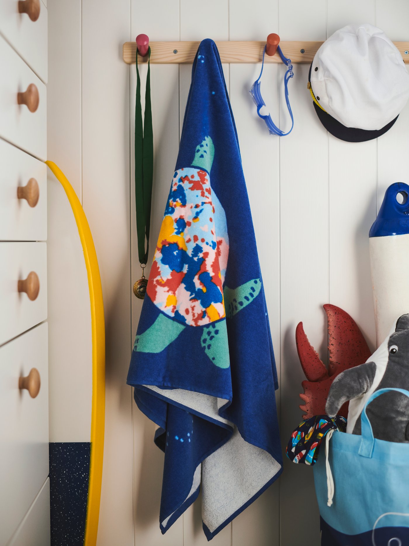 Una toalla de baño azul con estampado de colores cuelga de un perchero. Junto a la toalla hay una cómoda con seis cajones.