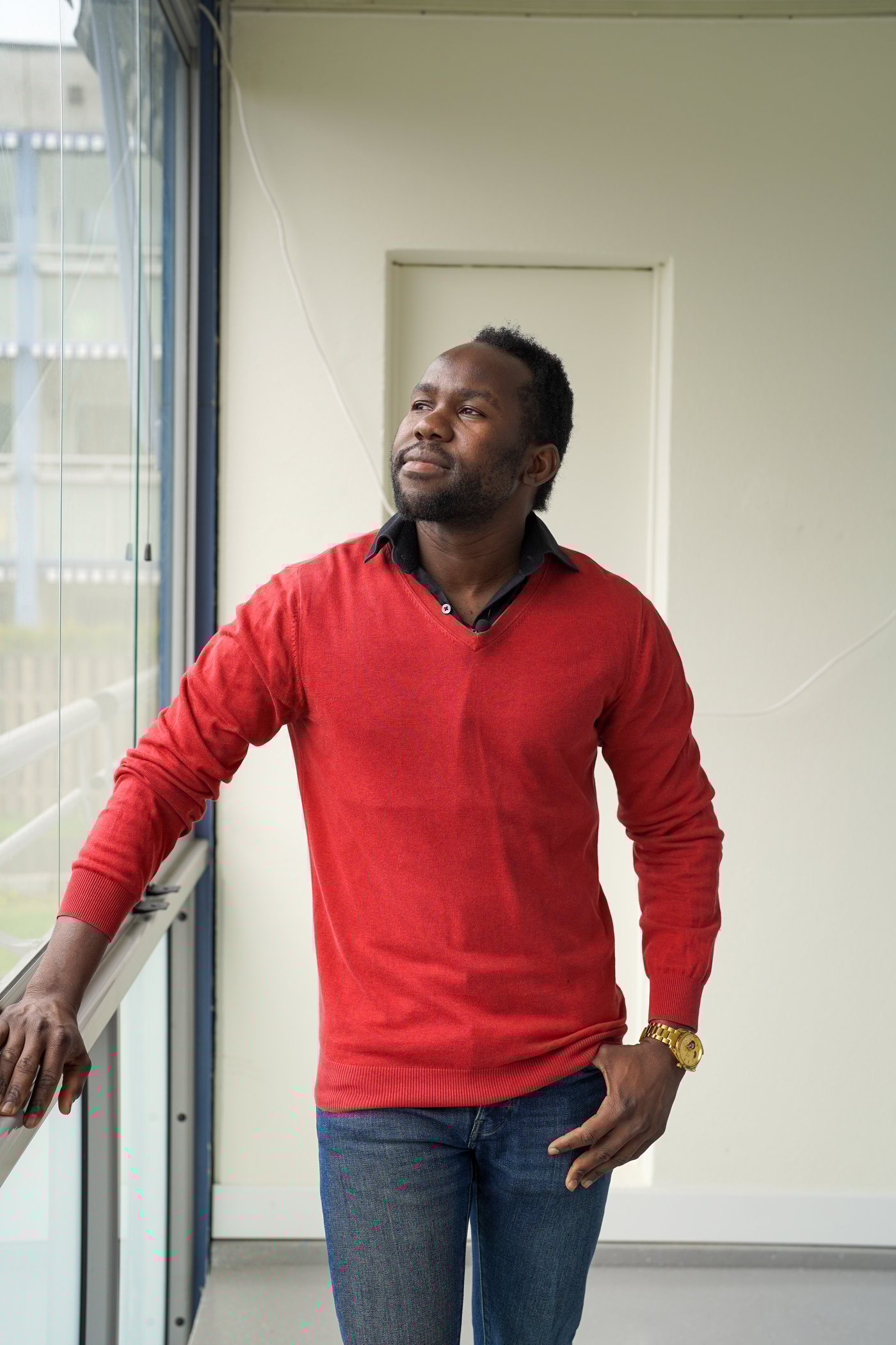 A man standing on a balcony in a red shirt looking out of the window.