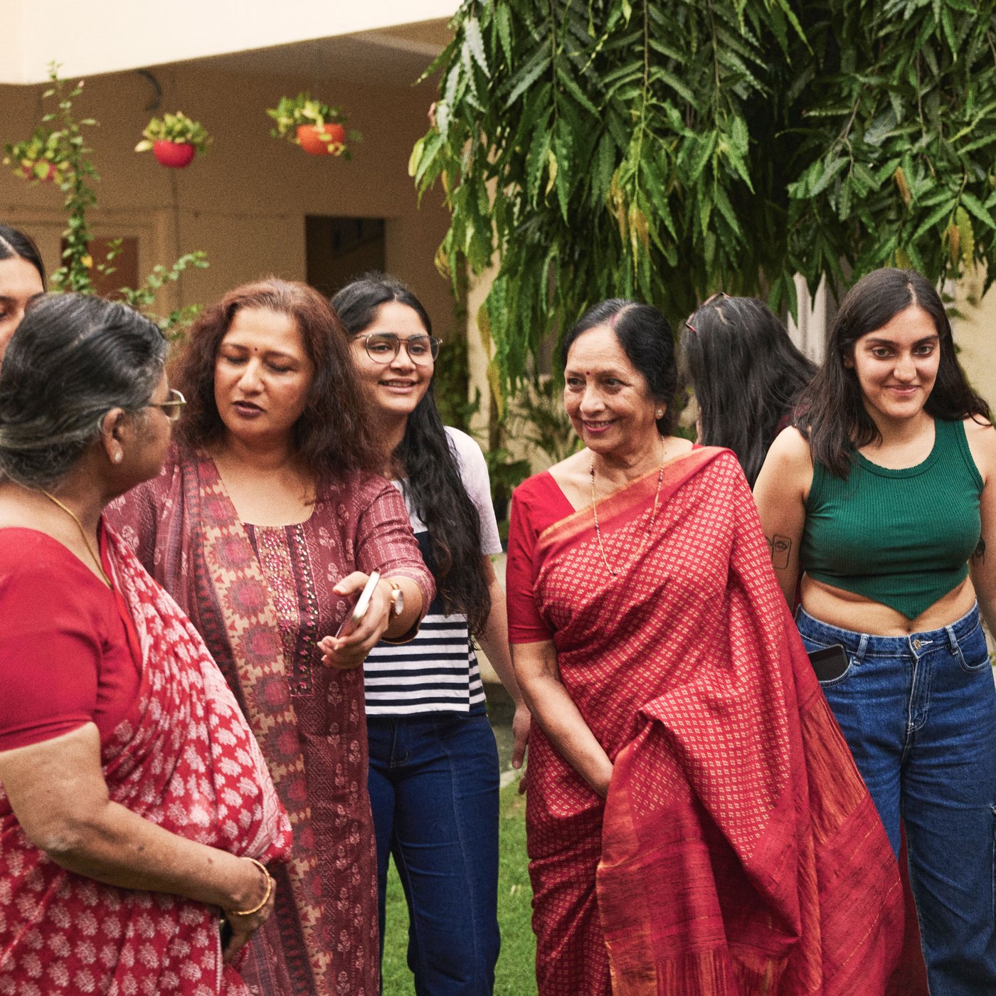 A group of women are standing in a garden in colorful clothes and socializing.