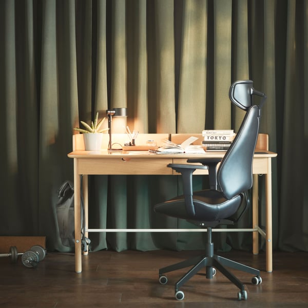 A workspace with a RIDSPÖ oak-veneer desk and a GRUPPSPEL gaming chair beneath wall-covering dark-green curtains.