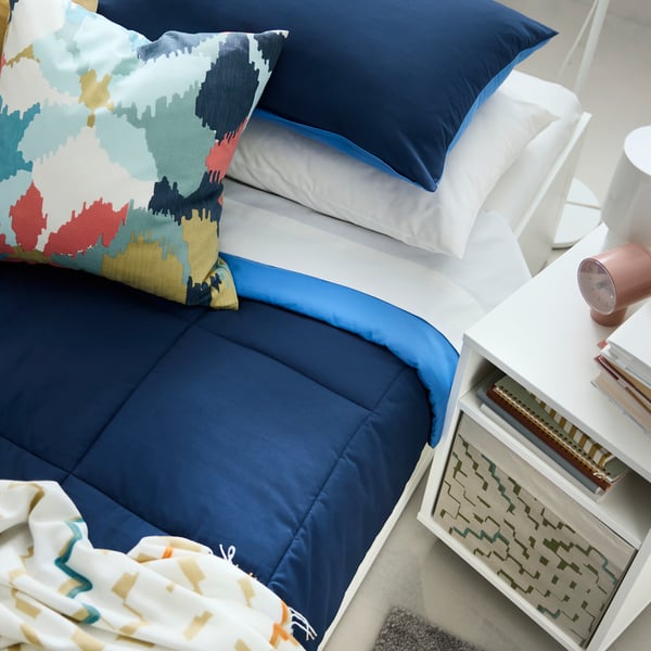 A BRIMNES day-bed with HEDFRYLE comforter and GAFFELFIBBLA cushion. Next to it, VIHALS bedside table with a DRÖNA box inside.