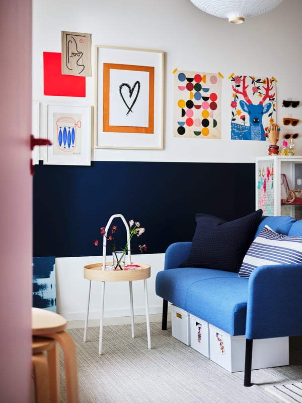 "In a living room, there is a blue sofa next to a TV, and above the TV, colorful pictures are hanging.
