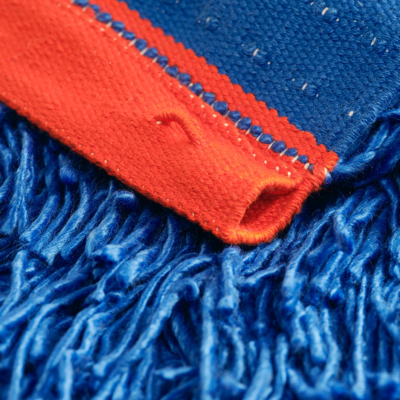Close up of a rug with long blue lashes and red details. The carpet is part of the IKEA KONSTRUNDA art collection.