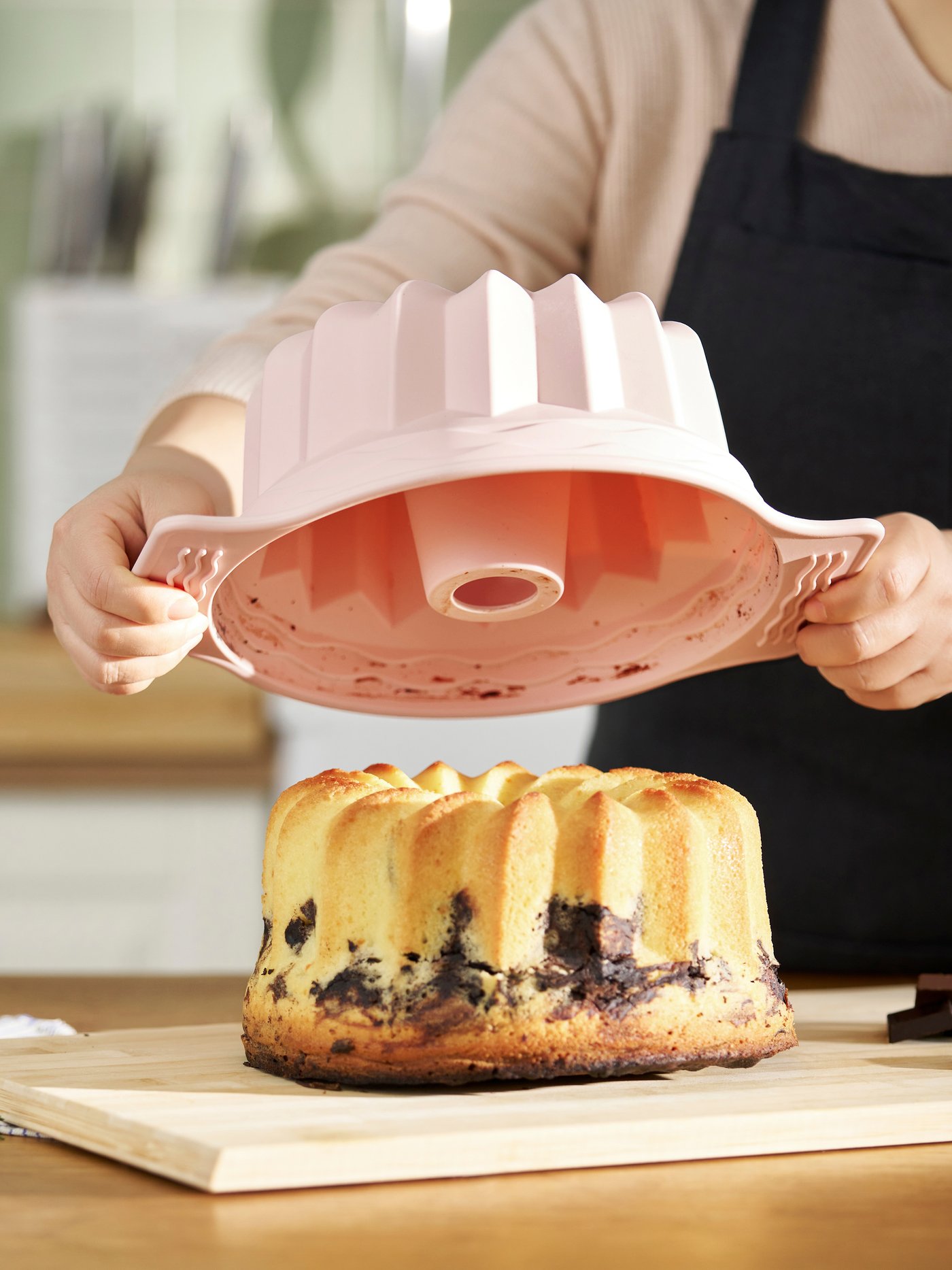 A person is lifting a pink cake tin, letting the cooked cake out.