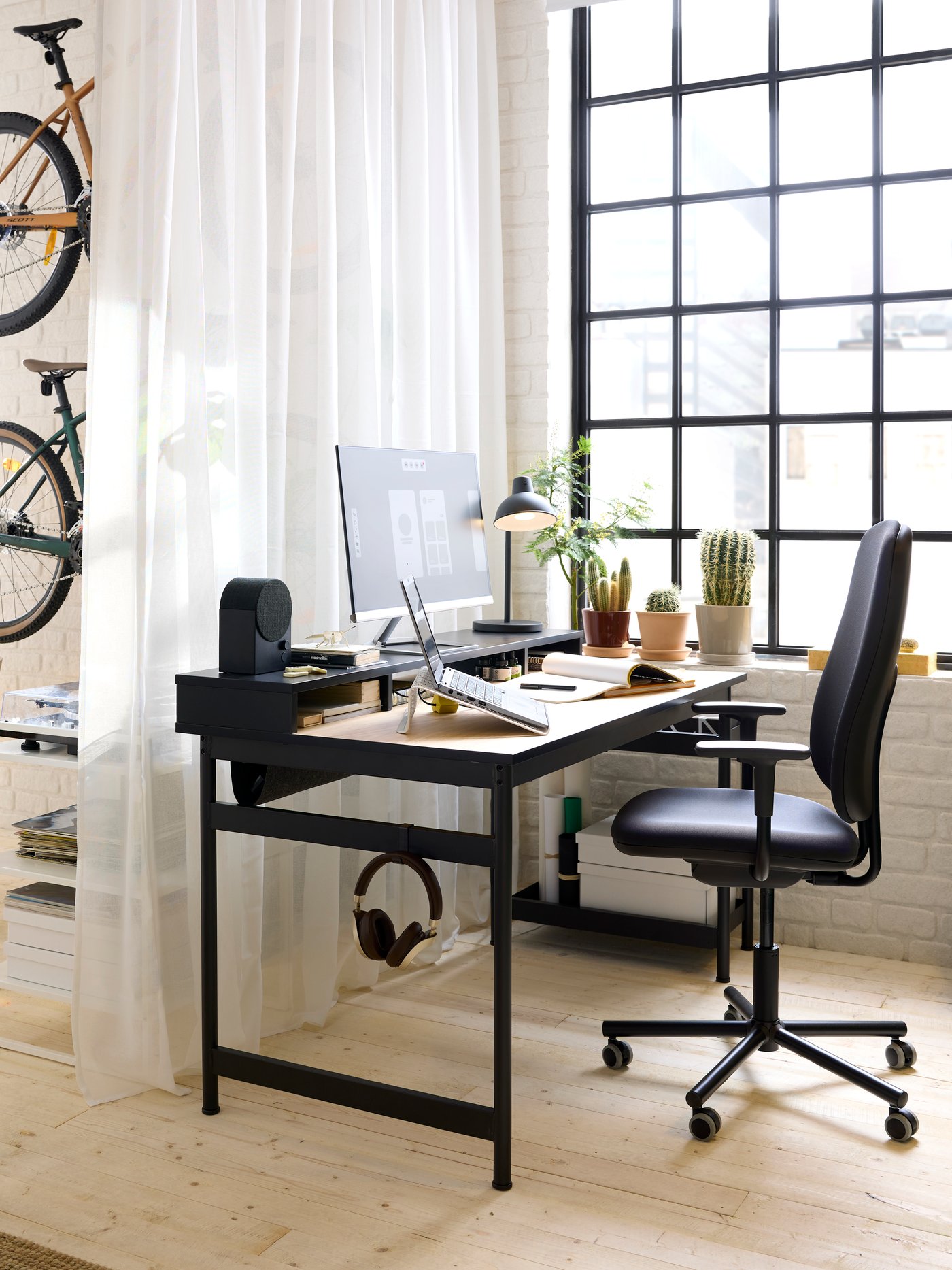A black MULLSJÖ desk with an oak top and a black Bluetooth speaker on the top unit. In front sits a SMÖRKULL office chair.