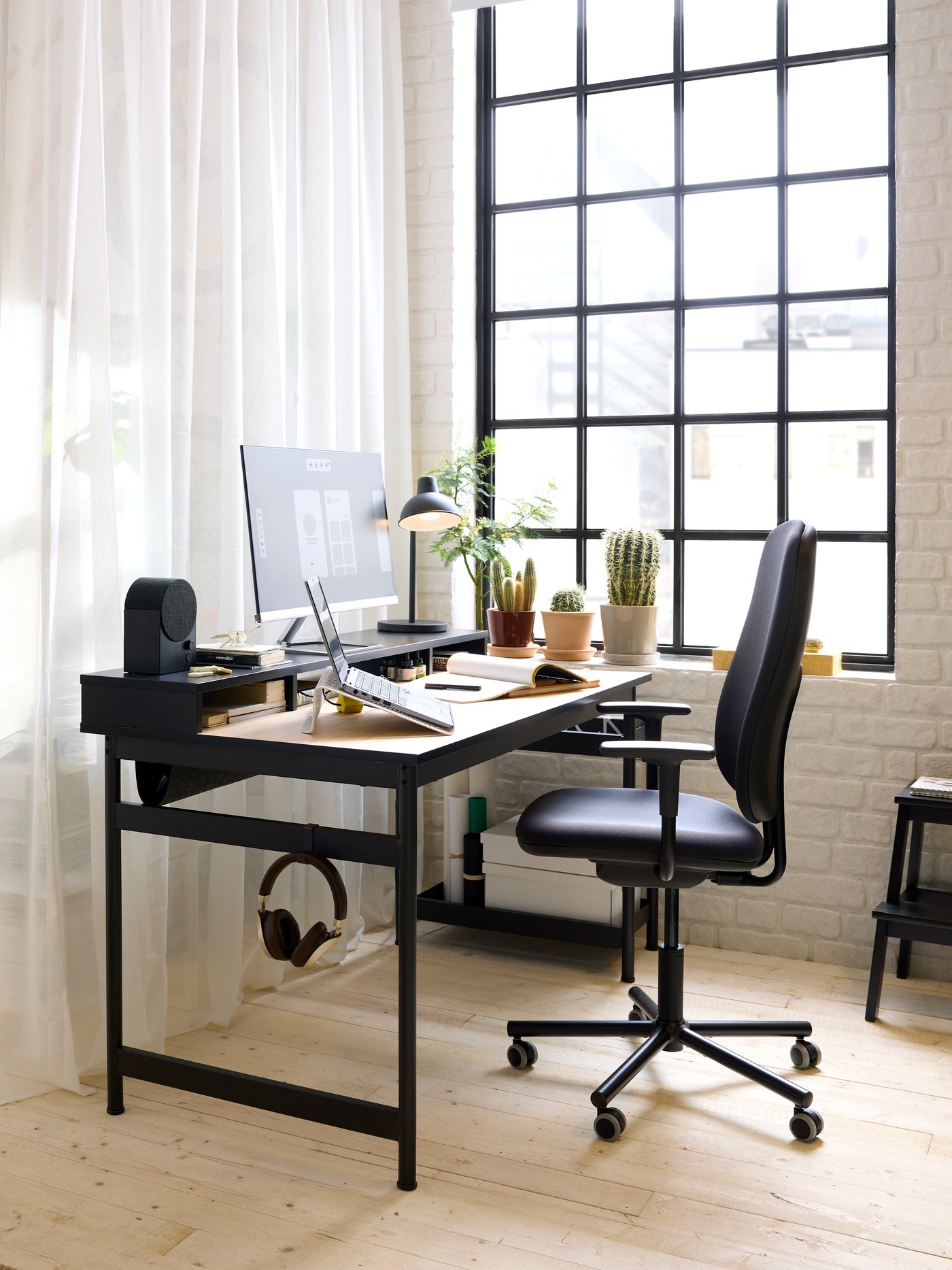 A black MULLSJÖ desk with an oak top and a black Bluetooth speaker on the top unit. In front sits a SMÖRKULL office chair.