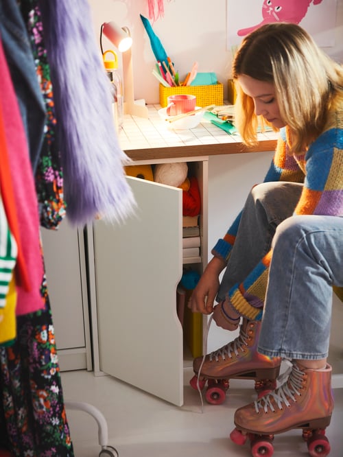 A children's room featuring a ALEX storage unit with a LAGKAPTEN table top and a person sitting next to it.