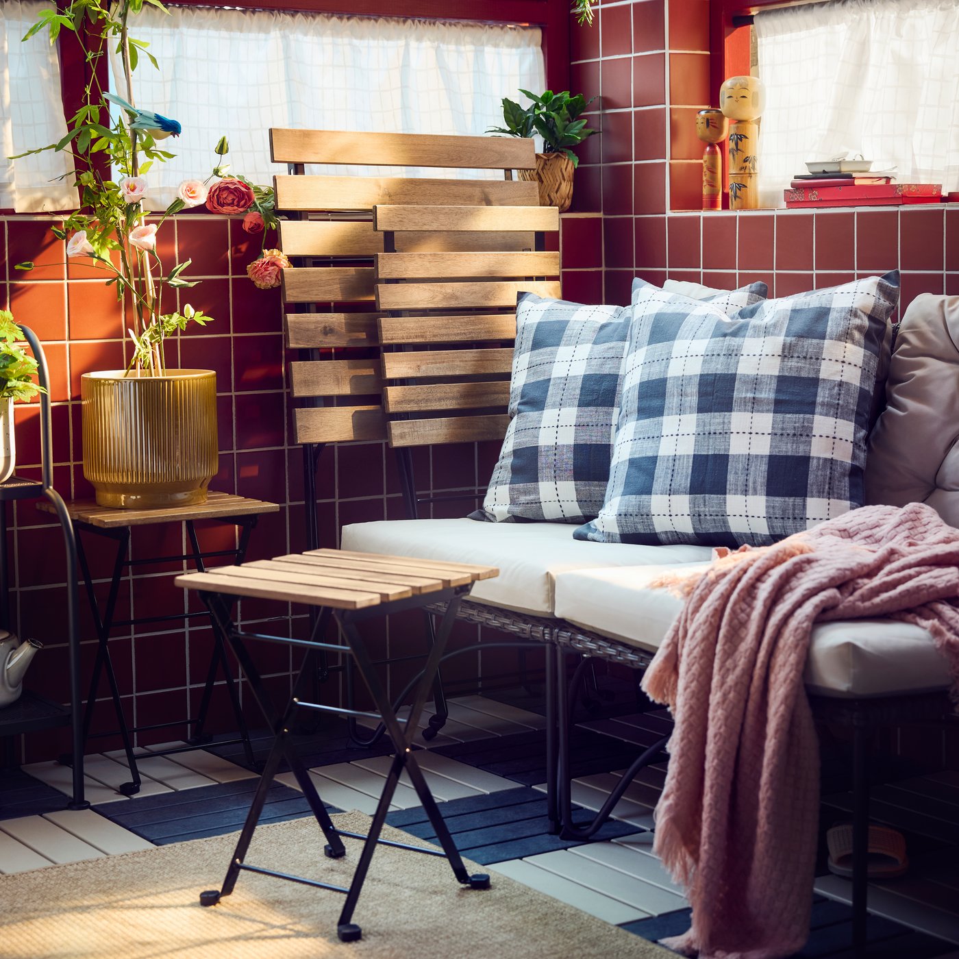 A balcony with dark grey JUTHOLMEN easy chair and light grey-beige cushions surrounded by patterned pillows and green plants.