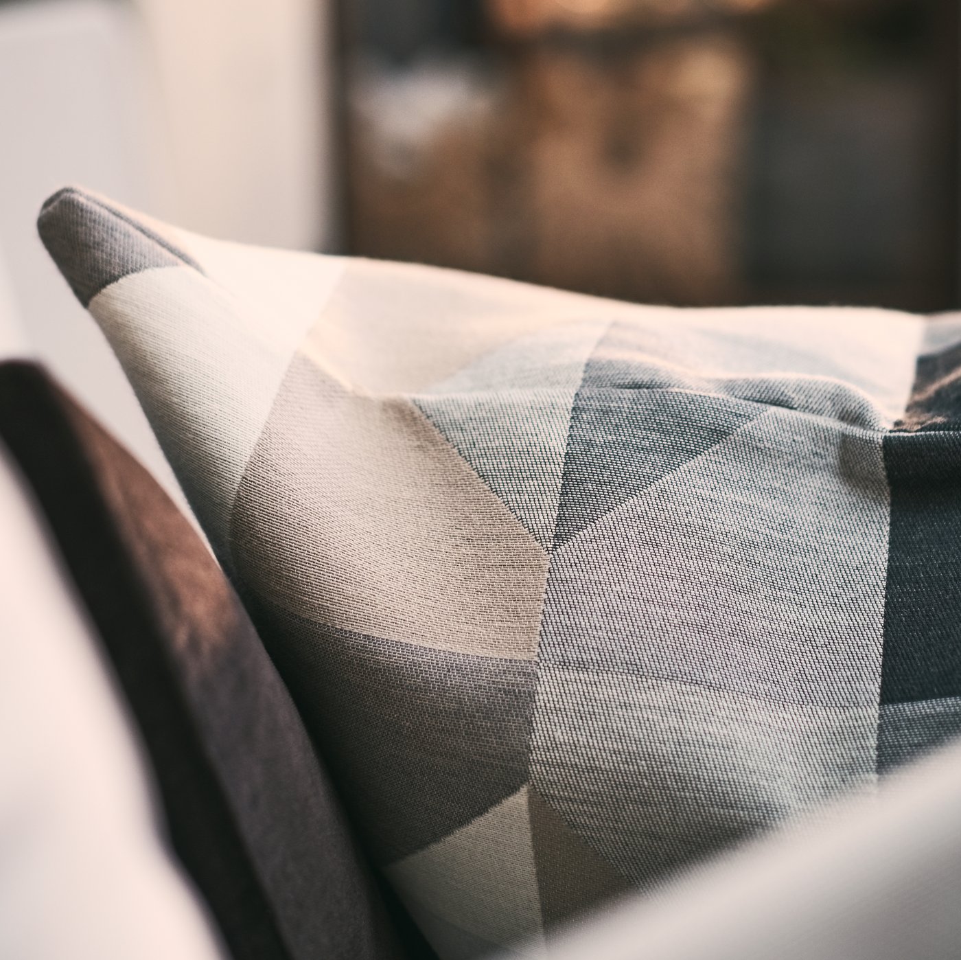 جانب من وسادة مغطاة بغطاء وسادة SVARTHÖ أخضر/أزرق على كنبة بلون فاتح.