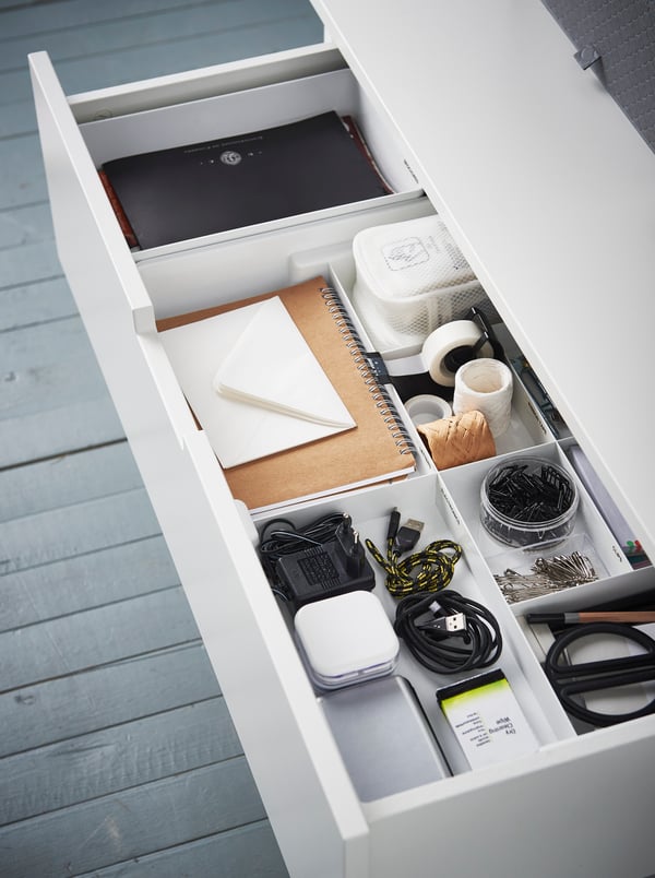 A KUGGIS insert with 8 compartments containing various stationery items, in an open drawer of a white chest of drawers.