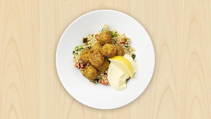 Falafelannos couscousin, vihannesten ja aiolin kanssa on katettu valkoiselle lautaselle.
