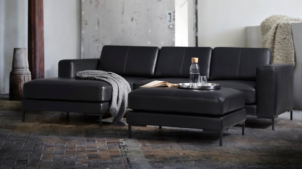 Leren voetenbankje FULLERÖ naast een zwarte leren bank