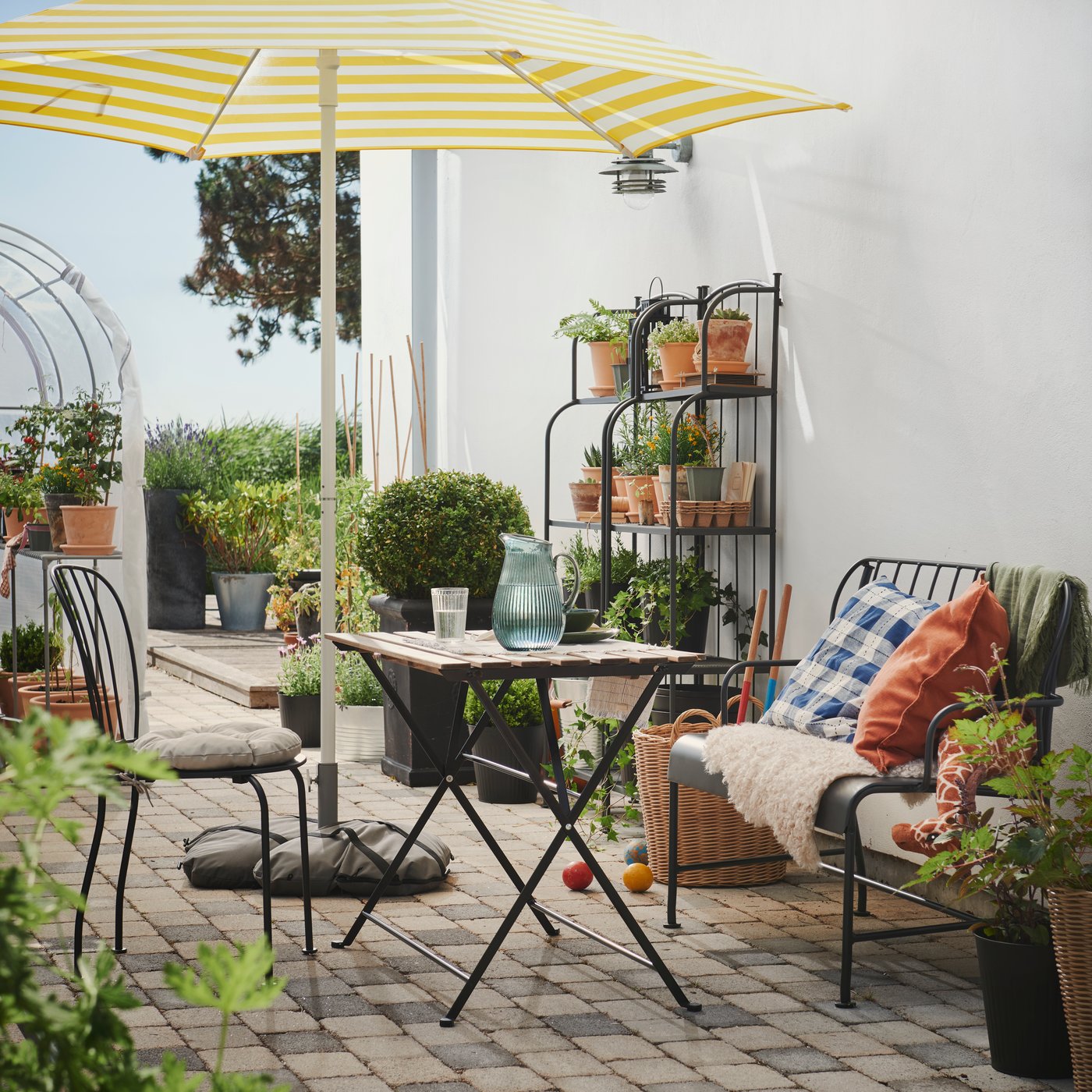 A bright outdoor patio with a black and light brown TÄRNÖ table, surrounded by chairs, a sofa and lush potted plants.