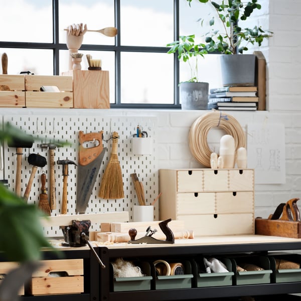 A light home woodworking station with two work benches, tools hung on SKÅDIS pegboards, and accessories in various boxes.