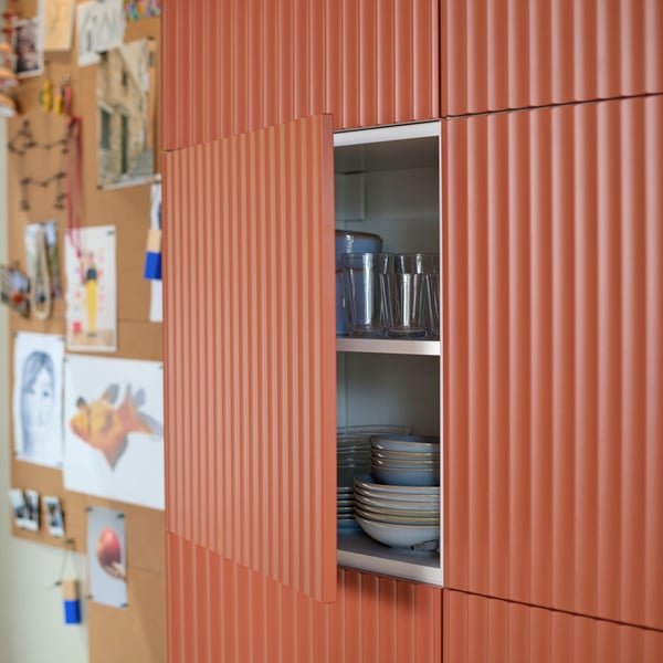 Une armoire de cuisine est dotée d'une porte décorative TERRSJÖ ouverte, avec un motif ondulé rouge-brun. Des ustensiles de cuisine sont rangés à l'intérieur.