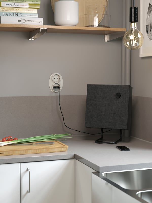 Un haut-parleur carré sur un comptoir gris avec dosseret assorti. Une tablette murale et un ensemble de câbles avec ampoule sont placés au-dessus.