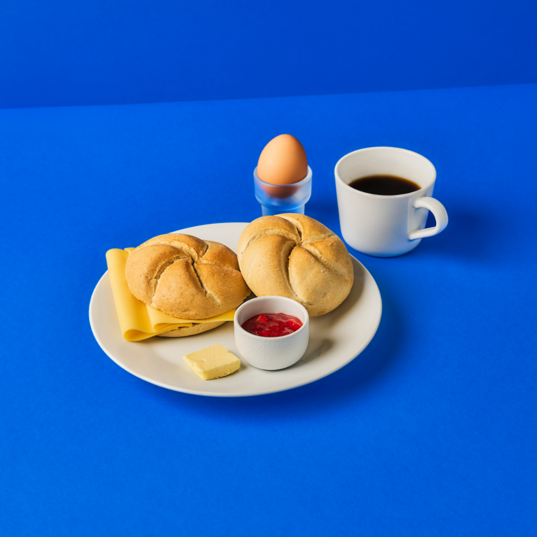 IKEA breakfast consisting of 2 kaiser rolls, 2 slices of cheese, a boiled egg, jam, and butter.