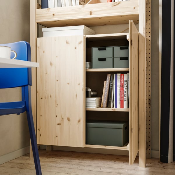 A bright space with an IVAR shelving unit, one pine cabinet door open to reveal books and storage boxes neatly arranged.