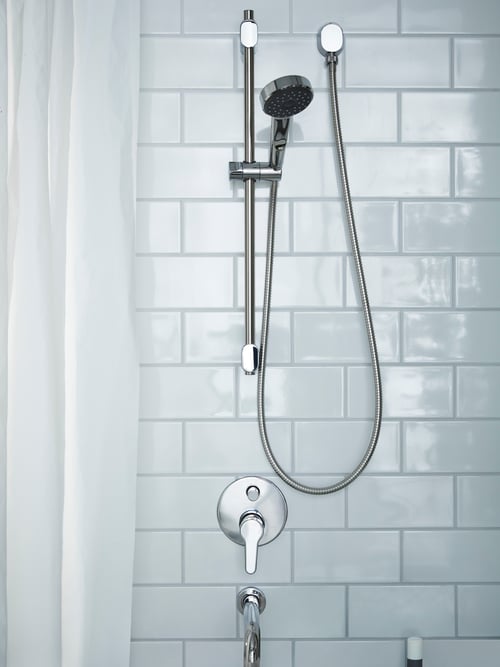 Gros plan sur une salle de bains minimaliste avec des carreaux blancs, un rideau de douche assorti et une douchette avec barre.