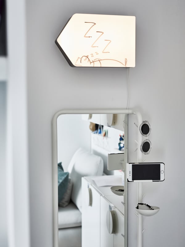 A lit wall lamp shaped like an arrow with a drawing of a sleeping person hangs above a full-length mirror.