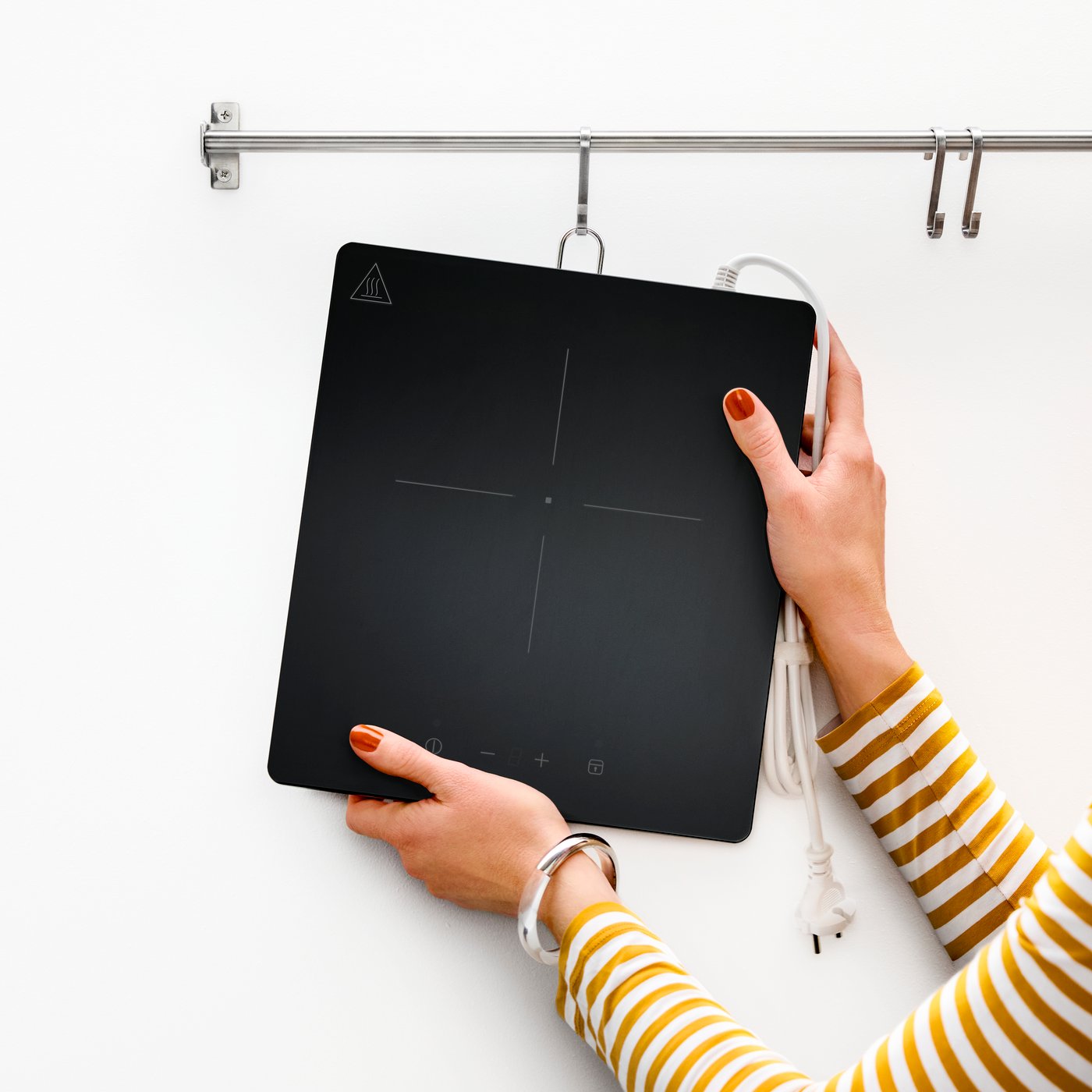 A person is hanging a portable TILLREDA induction hob on a hook on a rail.