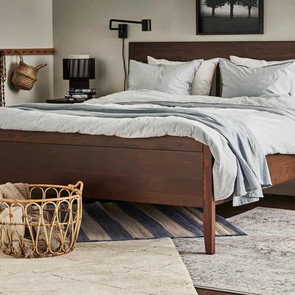 Tappeti VRENSTED, VEDBÄK e TVERSTED sotto un letto IDANÄS marrone scuro con biancheria BERGPALM blu/a righe e un plaid grigio.