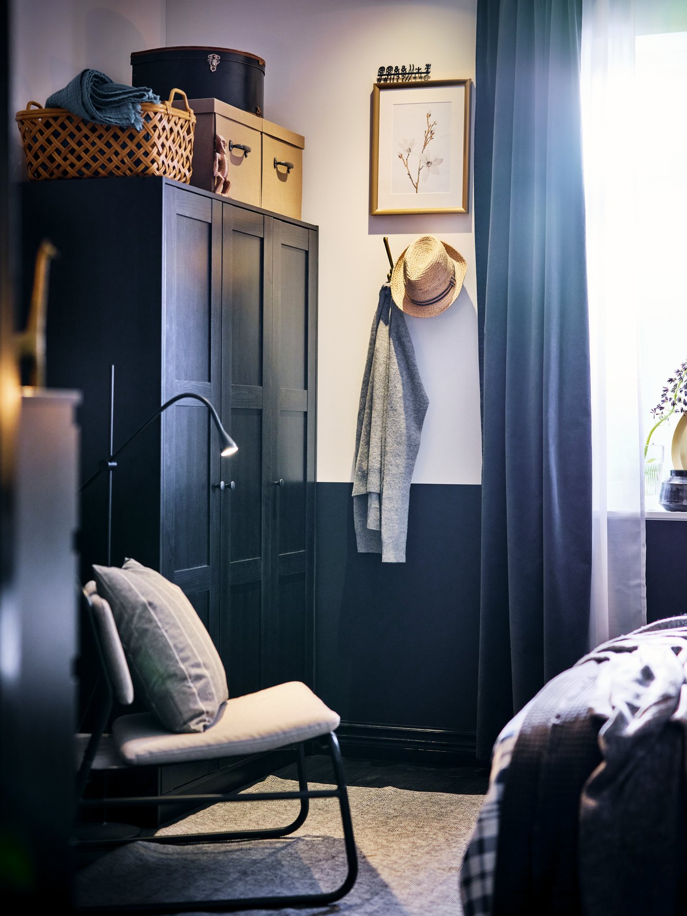 A corner of a bedroom with a black-brown RAKKESTAD wardrobe, a floor lamp and a light-grey LINNEBÄCK easy chair.