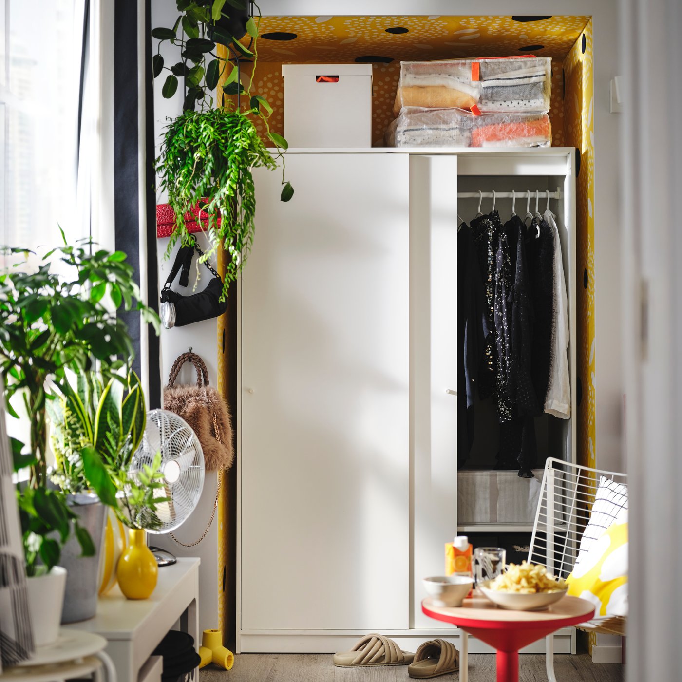 Une KLEPPSTAD armoire-penderie blanche à portes coulissantes est ouverte, révélant des vêtements suspendus et des boîtes de rangement bien rangés.