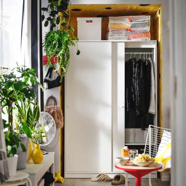 A white KLEPPSTAD wardrobe with sliding doors is open, showing neatly organised hanging clothes and storage boxes.