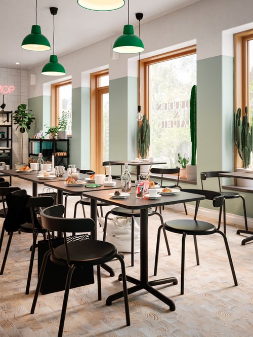 Dining area with multiple pendant lamps mounted over several square tables, chairs, and shelving units.