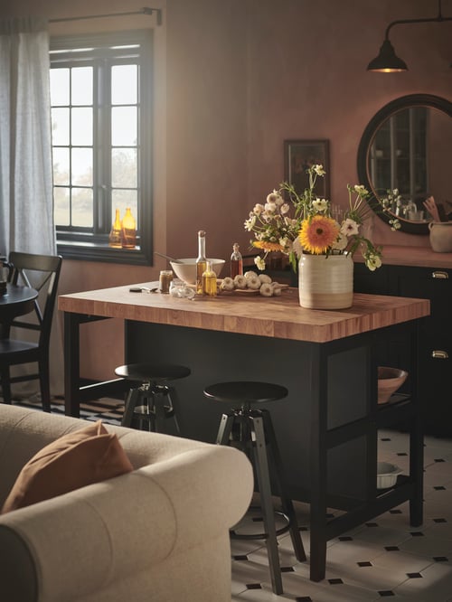 A modern kitchen that features a kitchen island, a 2-seat sofa, a white vase, a mirror, a bar stool, and a curtain rod.