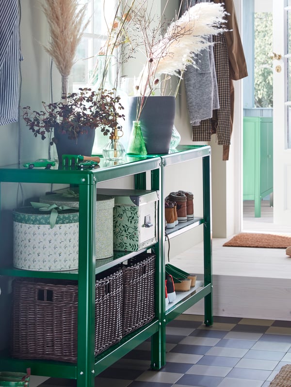 KOLBJÖRN shelving units stand by a window, holding FJÄLLA storage boxes, GABBIG baskets and shoes, with plants on top.