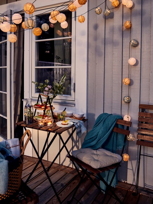 Dining room featuring a square table with 2 chairs for outdoor made of solid acacia wood, a serving tray and a grey throw.