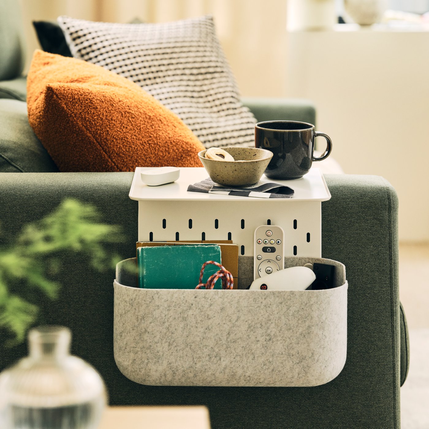 A softly sunlit space with a grey-green MALMKÖPING two-seat sofa with coffee accessories on a KRAMPHULT armrest tray.