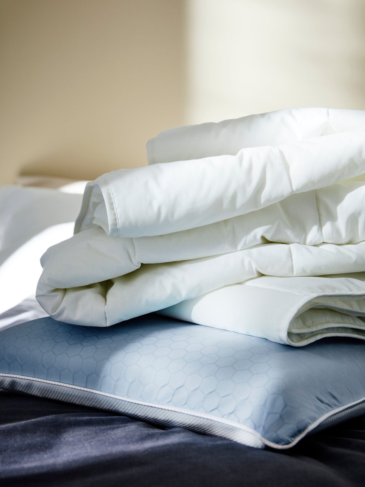 Zona de dormitorio con una almohada ergonómica azul sobre la que hay un edredón blanco parcialmente doblado.