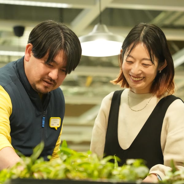 グリーン売場で、黄色とネイビーのユニフォームを着たイケアのコワーカー2人が植物を手に取りながら話している
