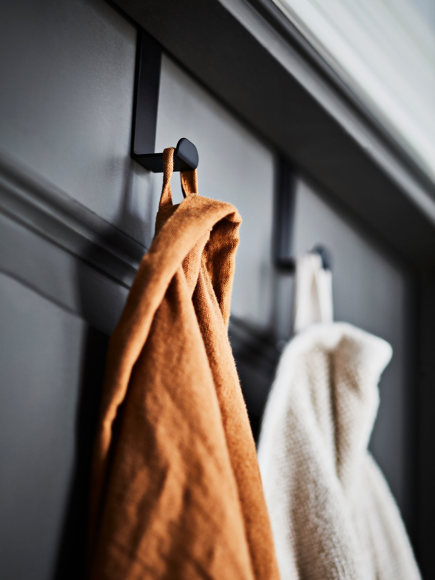 Detalle de un gancho SKOGSVIKEN negro para puerta con toallas de baño VINARN encima, en un ambiente de baño.