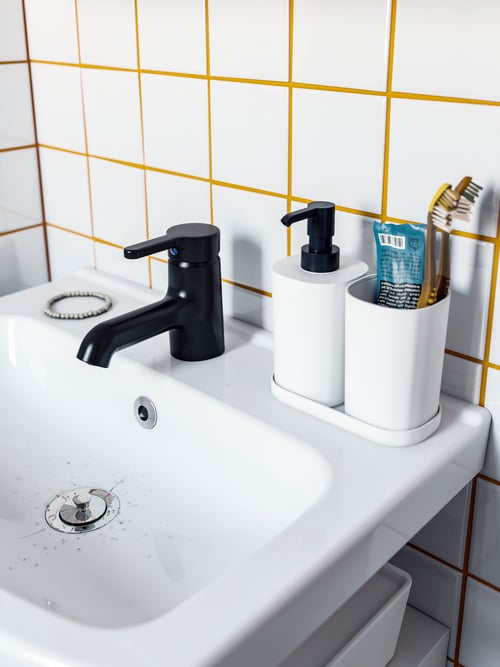 Baie cu un set de mobilier de baie din trei piese, un set de baie din cinci piese, gresie, periuțe de dinți și pastă de dinți, un robinet.