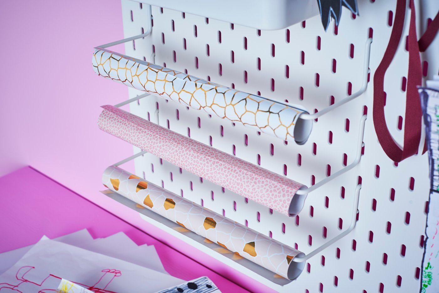 Eine weiße SKÅDIS Lochplatte an ihr sind Geschenkpapierrollen befestigt.