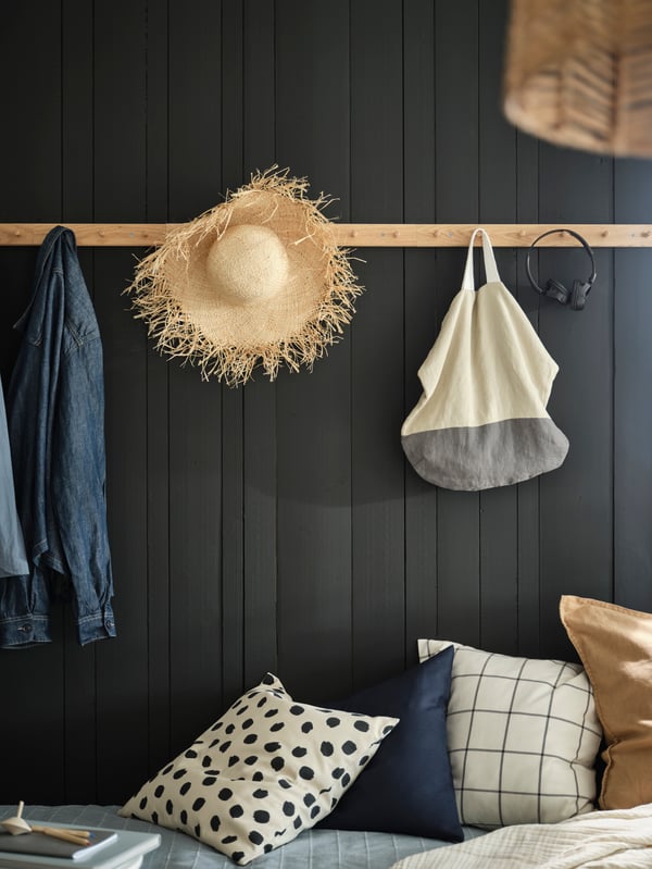 Une longue patère en bois avec boutons sur un mur foncé. Dessus sont accrochés une tête de téléphone, un chapeau, un sac en tissu et une veste en jeans.