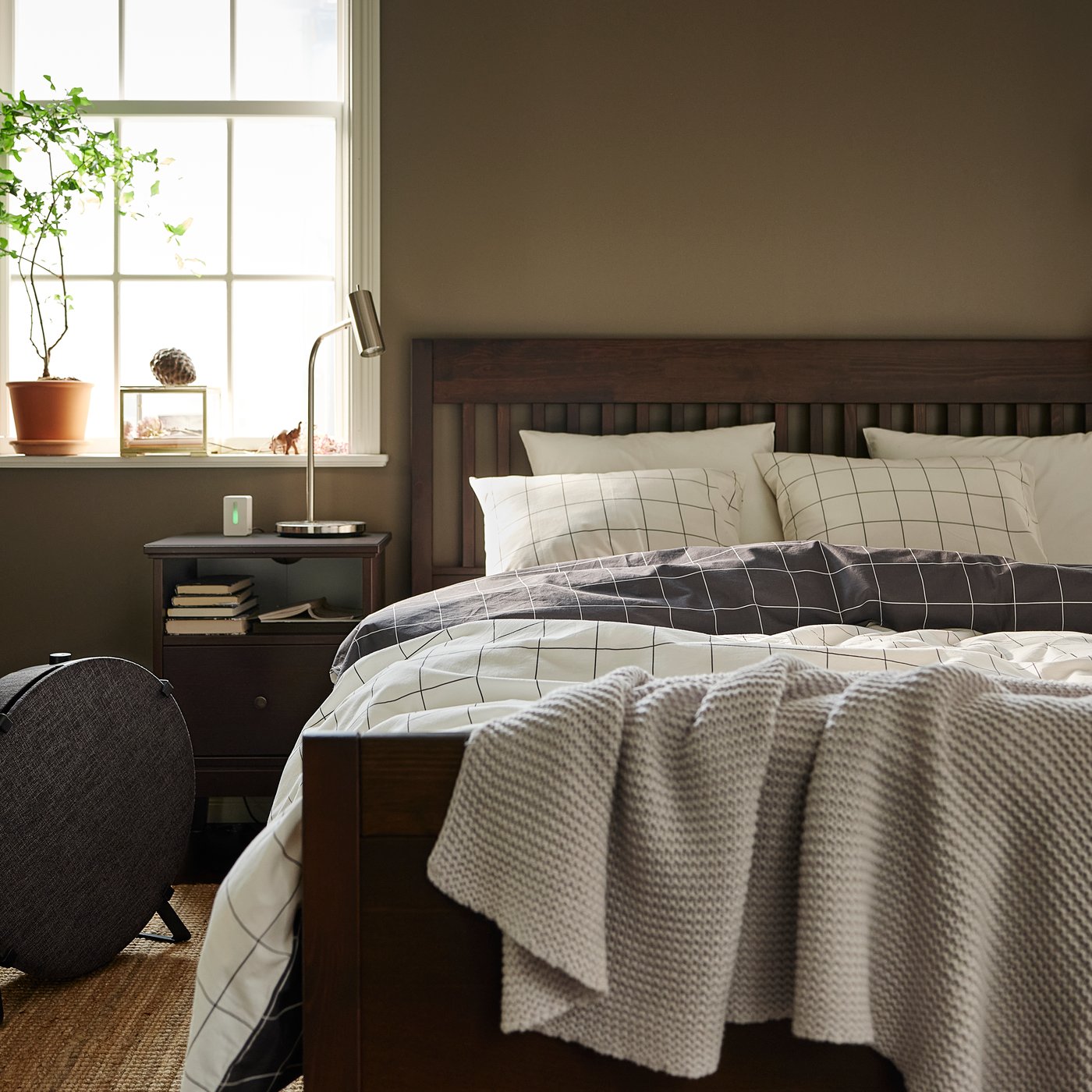 Struttura del letto in legno scuro con testiera a doghe in una camera da letto grigia in stile tradizionale con lenzuola a quadri grigio scuro e bianco e coperta lavorata a maglia - IKEA