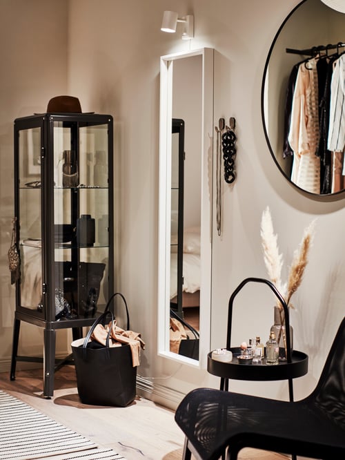Two mirrors, a tall NISSEDAL and a round LINDBYN, hang on the wall close to a dark grey FABRIKÖR glass-door cabinet.