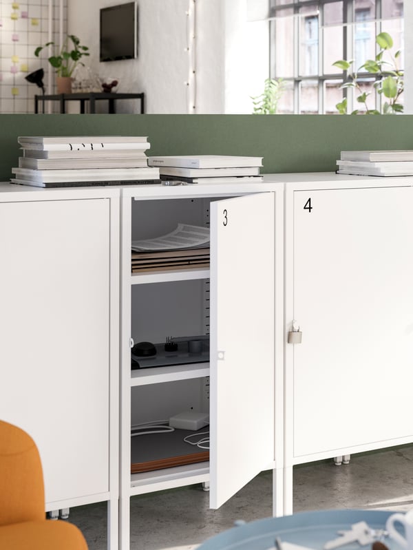 A row of white lockable cabinets with numbers on them, with one door is open showing papers and other items inside.